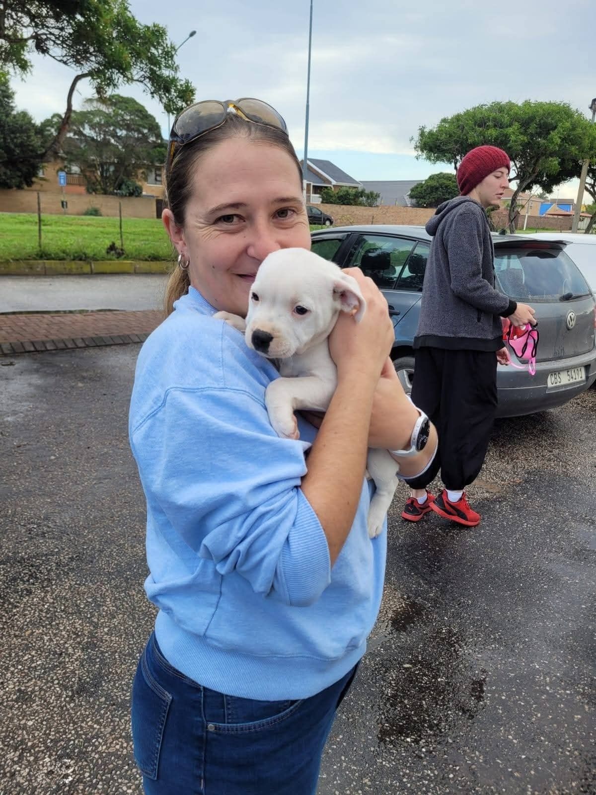 A new owner holding her white puppy on the pavement
