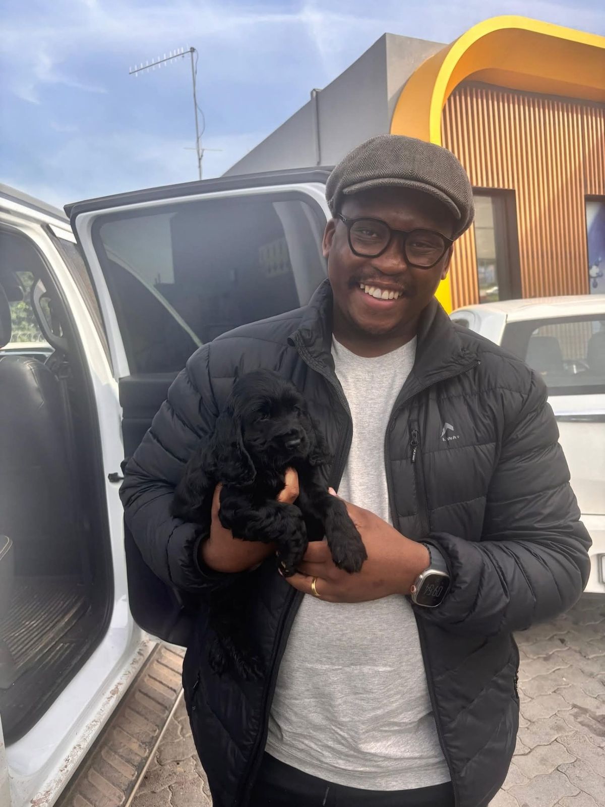 A man collecting his black puppy beside the vehicle