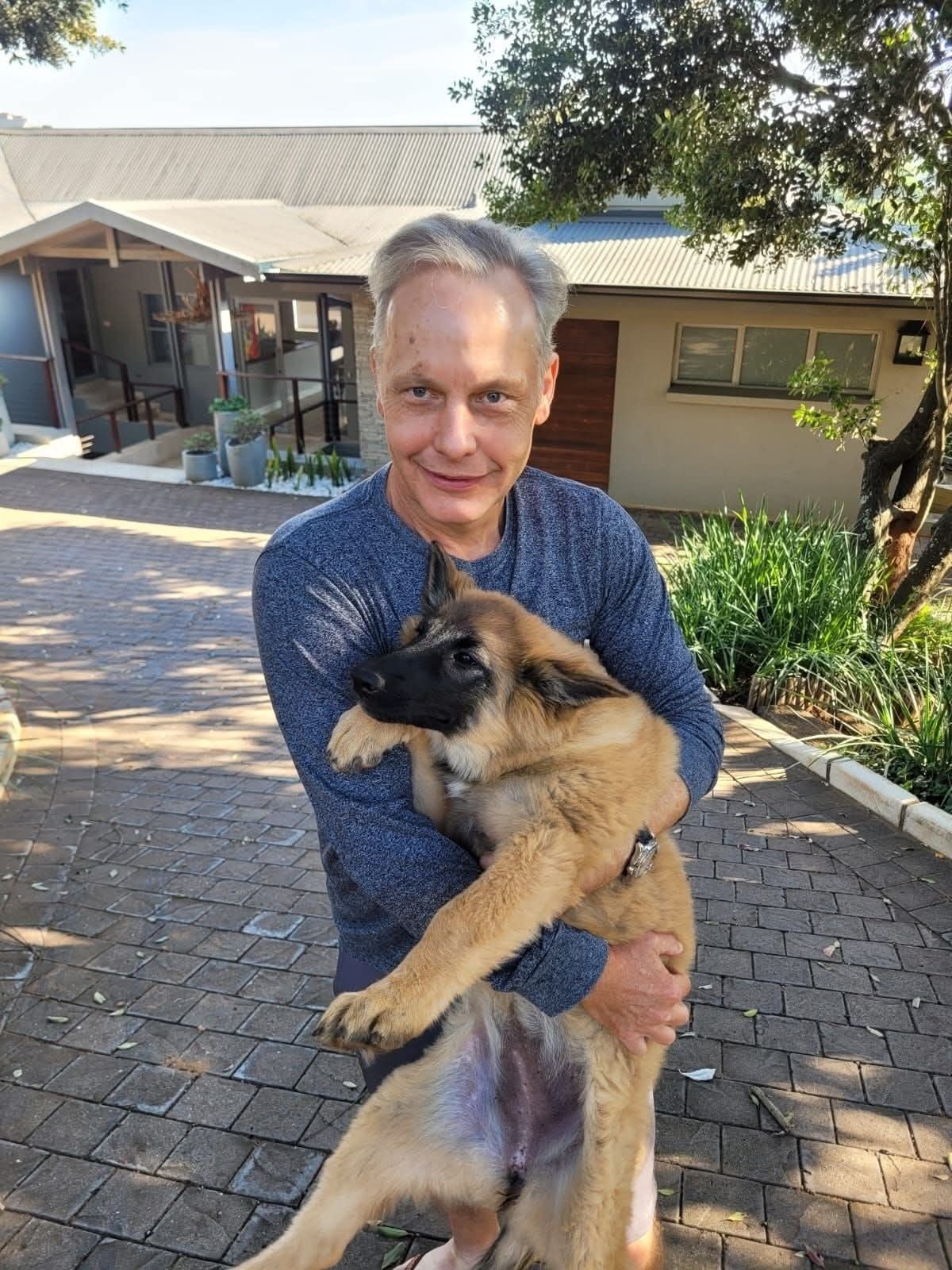 An older gentleman with his fawn puppy on the driveway