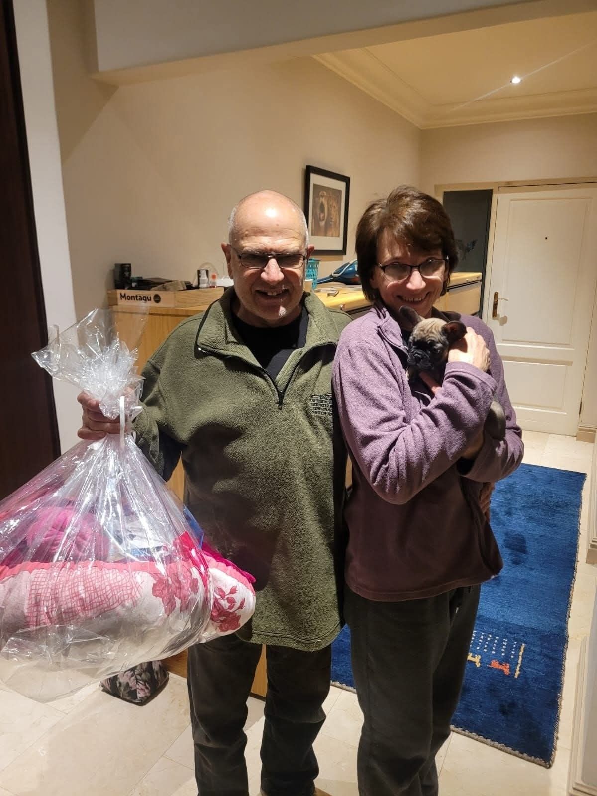 An older couple indoors with their puppy and welcome bag