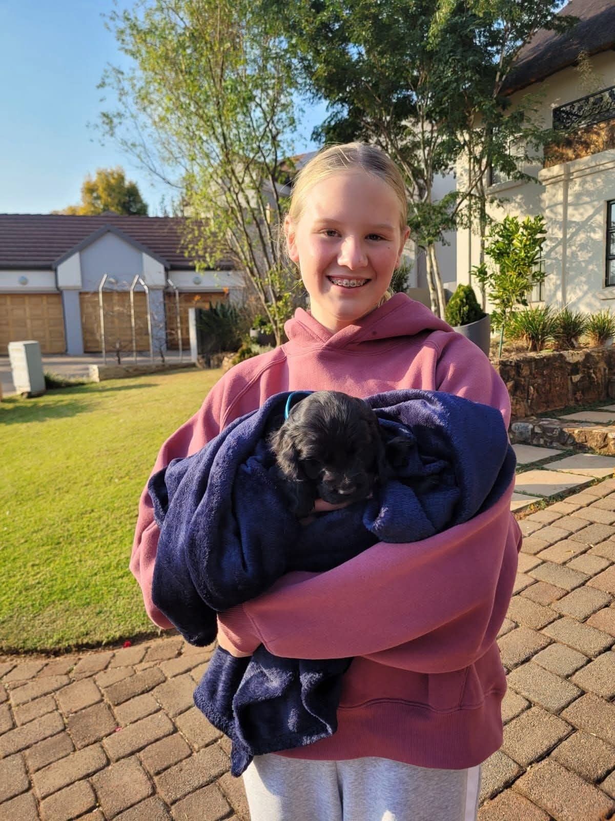 A girl in pink with her dark puppy wrapped in a blanket