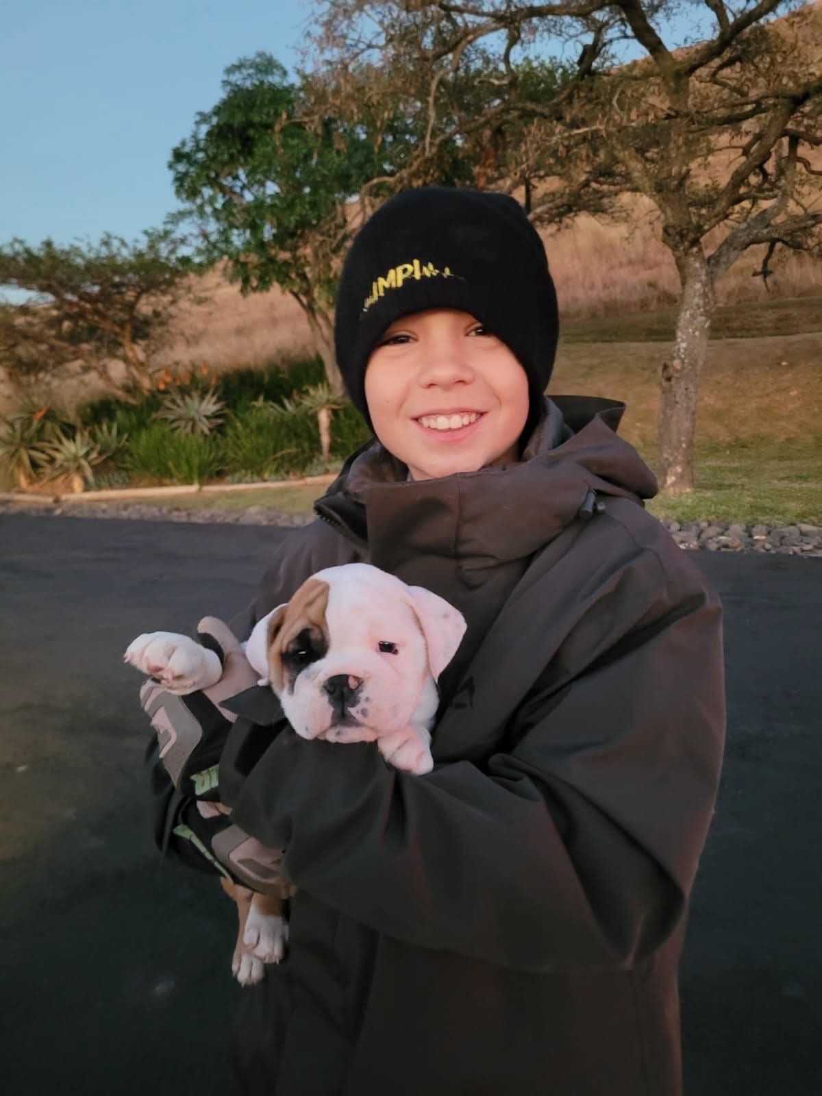 A young owner in a beanie with his white and brown puppy
